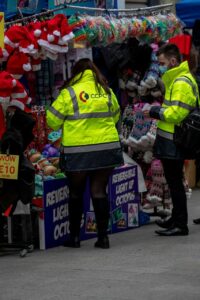 Two CCPC Authorised Officers in branded hi-vis jackets inspecting children’s toys for sale at an outdoor market stall.