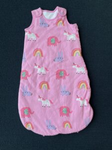 A image shows a pink animal-patterned baby sleep bag a, lying flat on a surface. 