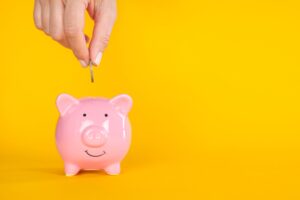 Image shows a hand adding a coin into a piggybank.