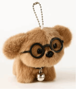 A small, light brown plush toy shaped like a dog with round black glasses and a shiny silver bell attached to its neck. The toy has large, round black eyes and a short snout. A metallic ball chain is attached to the top of its head, suggesting it can be used as a keychain or bag charm.