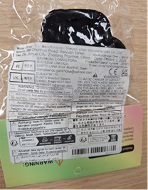 The back of the same package showing a white label with dense printed text in black. It includes manufacturer details, safety warnings, compliance symbols (CE, recycling icons), and multilingual instructions. The squishy toy is partially visible through the clear plastic, appearing black from this angle.