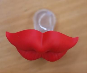 A novelty pacifier with a bright red rubber attachment shaped like cartoon-style lips. The pacifier has a transparent mouthpiece.