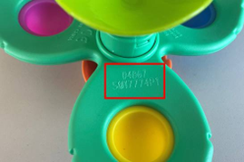 Close-up of a green plastic toy with a yellow circular center. A red rectangle highlights where to find the batch number of the product.