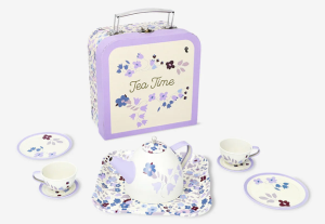 A children's floral-patterned toy tea set displayed with a matching carry case. The set includes a white teapot with purple and blue flowers, two small teacups with saucers, two plates, and a rectangular tray, all featuring coordinating floral designs. The upright carry case behind the set is cream and lavender with the words ‘Tea Time’ and matching flower illustrations.