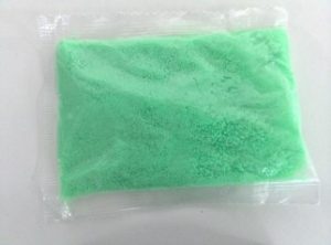 A small sealed transparent plastic packet containing bright green play sand, placed on a white surface.