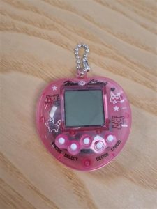 Transparent pink heart-shaped electronic toy with a small square screen and 5 small white buttons
