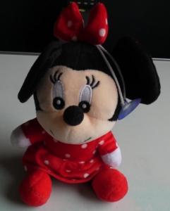  A small plush toy shaped like a cartoon-style mouse sitting upright. The toy wears a red outfit with white polka dots and a matching bow on the head. The plush has black ears, embroidered eyes, and a soft fabric texture. A small hanging loop with a suction cup is attached to the side of the head. 